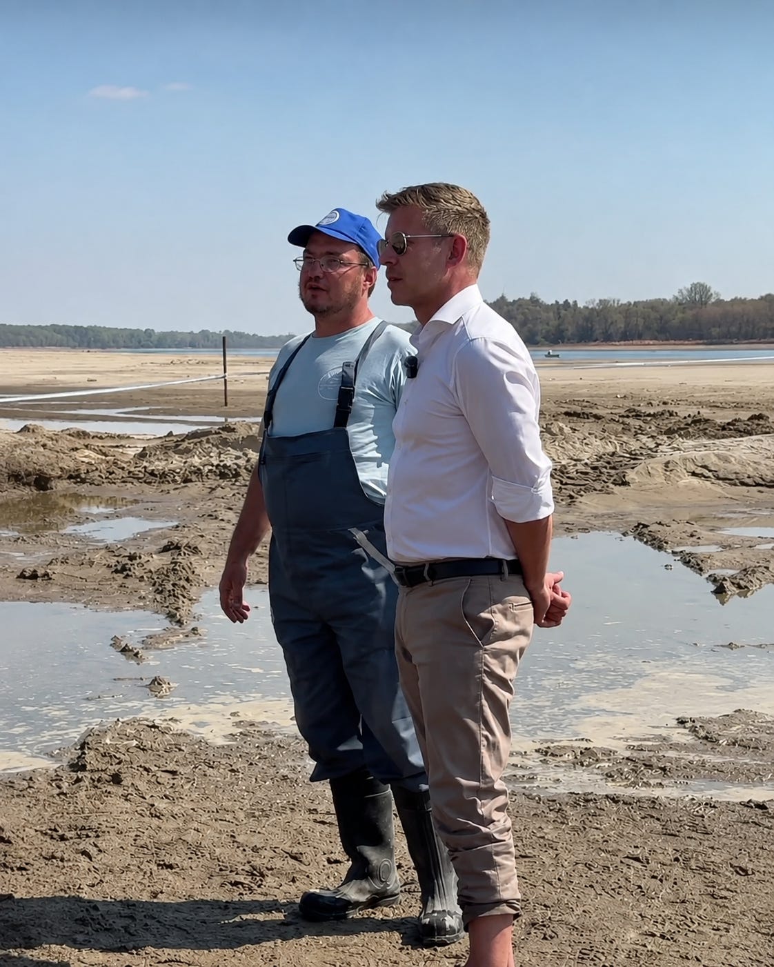 Péter Magyar stands barefoot on the exposed Danube riverbed near Paks beside a worker as exceptionally low water levels reveal large stretches of the riverbank. Péter Magyar stands barefoot on the exposed Danube riverbed near Paks beside a worker as exceptionally low water levels reveal large stretches of the riverbank.