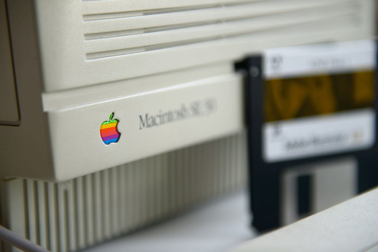 A Macintosh SE 30 desktop computer from the late 1908s, together with a floppy disk containing Adobe Photoshop.
