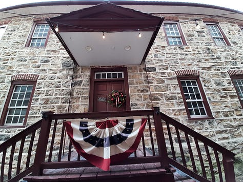 Pictures from Bethlehem, Pa., starting with the oldest waterworks in the United States, built in the 1700s. It's a stone building with cloudy sky. Next picture is three carriage horses standing in front of the 9-story tall brick Hotel Bethlehem, and a historic stone building that was used as a hospital during the Revolutionary War. Middle row is the Sun Inn Tavern, where almost all of our Founders ate and gathered at one time or another, The building is stone and there is white picket fence in the back and a porch with a red, white and blue banner on the side. Bottom row: Bethlehem's industrial park with original buildings made of stone against a blue sky. Last photo is the blacksmith busy at work in the blacksmith shop with a blazing fire.