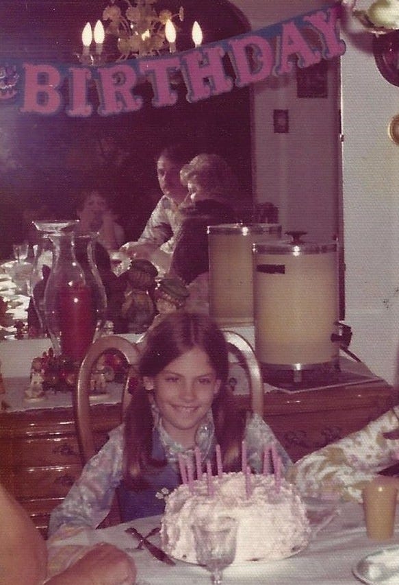 10-year-old girl listens as a band of relatives around a dining room table sing happy birthday before she blows out the candles on her cake