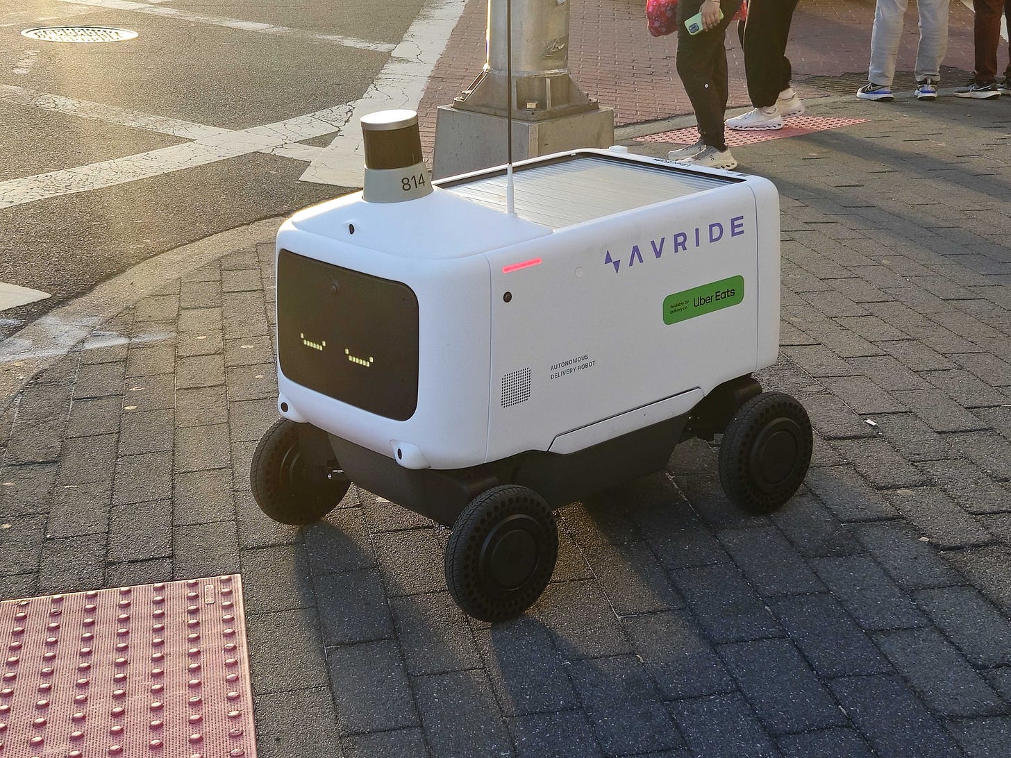 A photo of an Uber Eats autonomous delivery robot on a sidewalk during the day. A photo of an Uber Eats autonomous delivery robot on a sidewalk during the day.