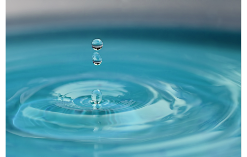 Two droplets of water hang suspended over a pool of water after a drop has splashed down. Ripples circle the area where the drop landed.