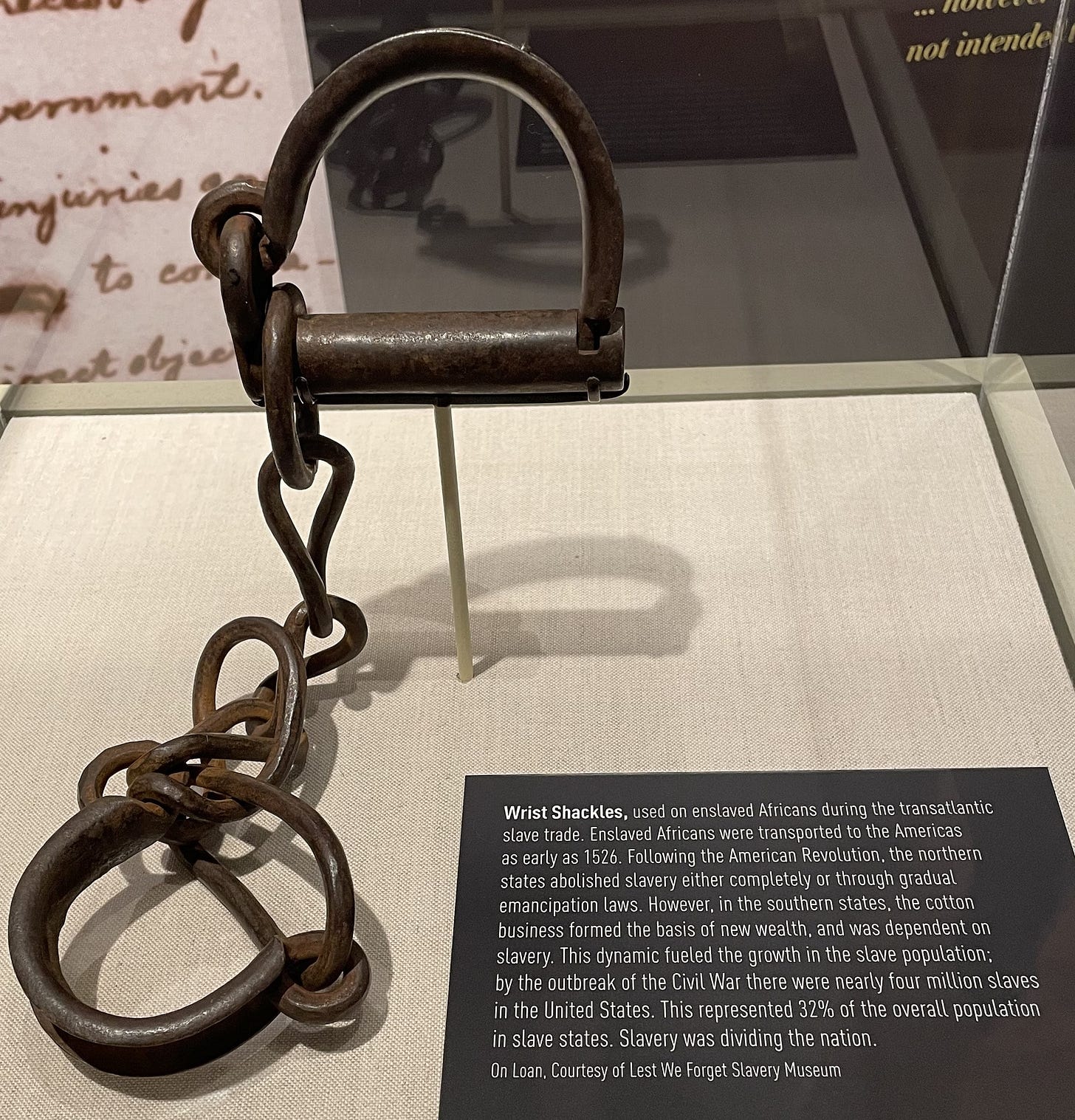 Iron wrist shackles in display case with accompanying museum label. Iron wrist shackles in display case with accompanying museum label.