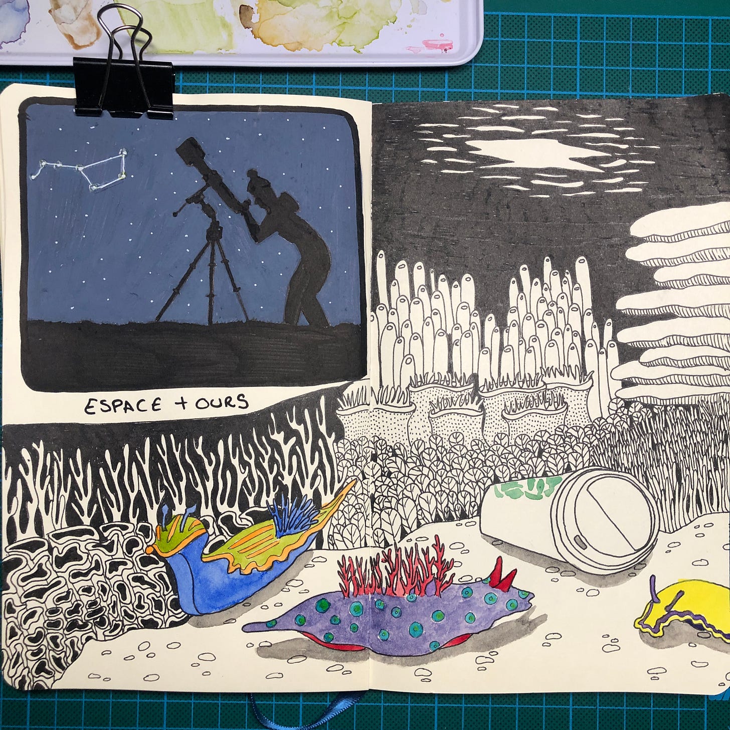 Photo de mon sketchbook : dans le quart en haut à gauche on voit mon dessin du jour 11 réalisé entièrement aux marqueurs Posca. Le reste de la double-page est consacré au dessin du jour 12 réalisé au stylo-plume, encre noire et un peu d'aquarelle. On voit un gobelet de café au logo vert au fond de la mer, trois nudibranches colorés et un décor de coraux en noir et blanc.