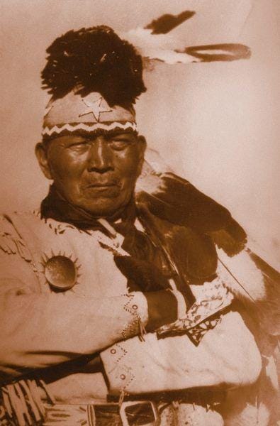 This may contain: an old photo of a native american man with feathers on his head and in traditional clothing