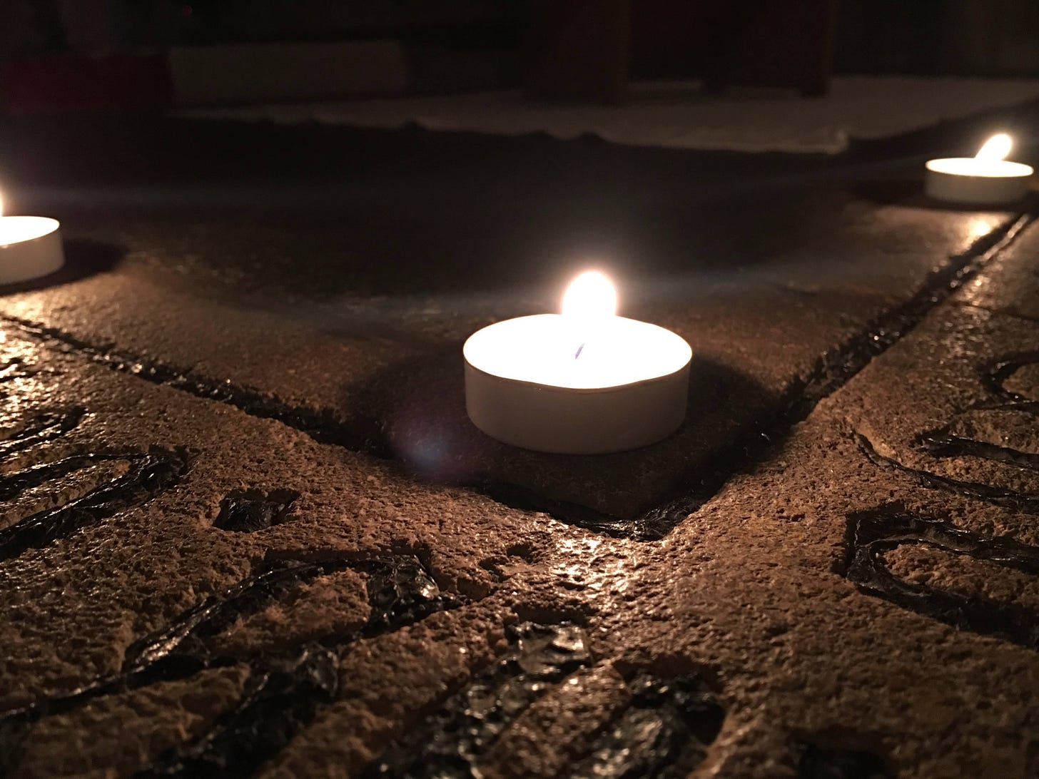 A single lit candle burns softly in a darkened space, its warm flame casting gentle light into the surrounding shadows.