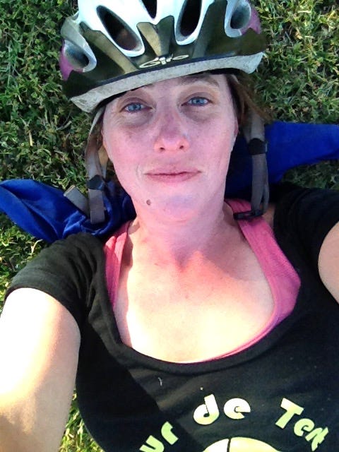 A selfie of the author lying in grass, bicycle helmet still on, wearing a tired and satisfied expression, after a long ride