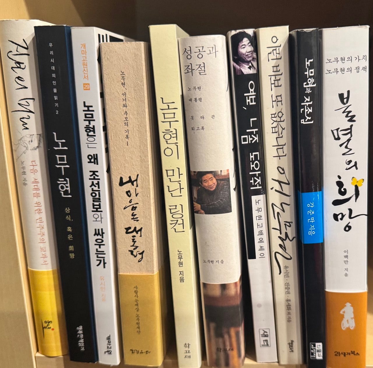 A close-up photo of a bookshelf lined with Korean-language books by and about former South Korean President Roh Moo-hyun, including several spines featuring his name and portrait.