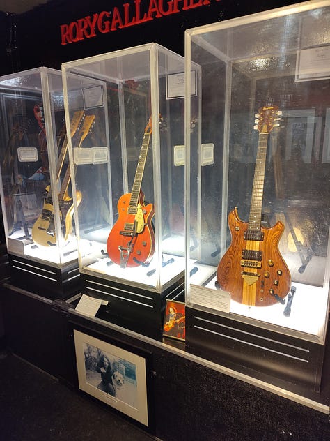 Five photos from the Irish Rock and Roll Museum and Temple Bar district. First, my daughter next to a photo of the band, U2. A display of three vintage guitars. The museum's Wall of Fame exterior and a streetscape in Temple Bar.