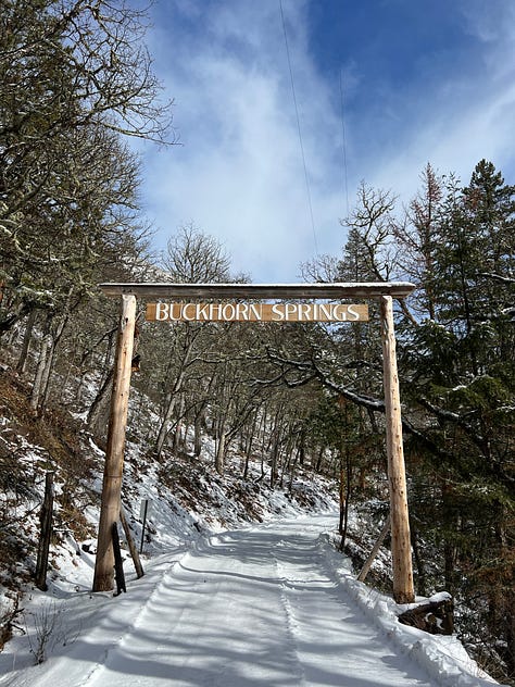 Main lodge covered in snow; inside the yoga yurt; partner yoga; cabin interior; the group, enjoying dinner; a bunch of smiling yoga friends; two friends on a bridge; two friends enjoying sledding; Buckhorn Springs welcome sign