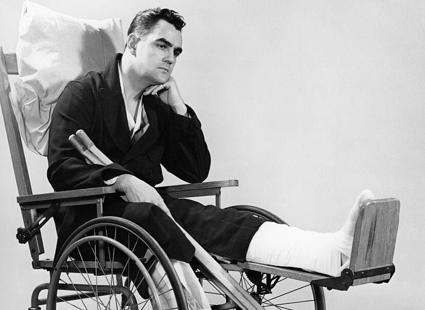 A photo from the 1940s of a man in a wheelchair, one leg in a cast propped up and a pillow behind his back.