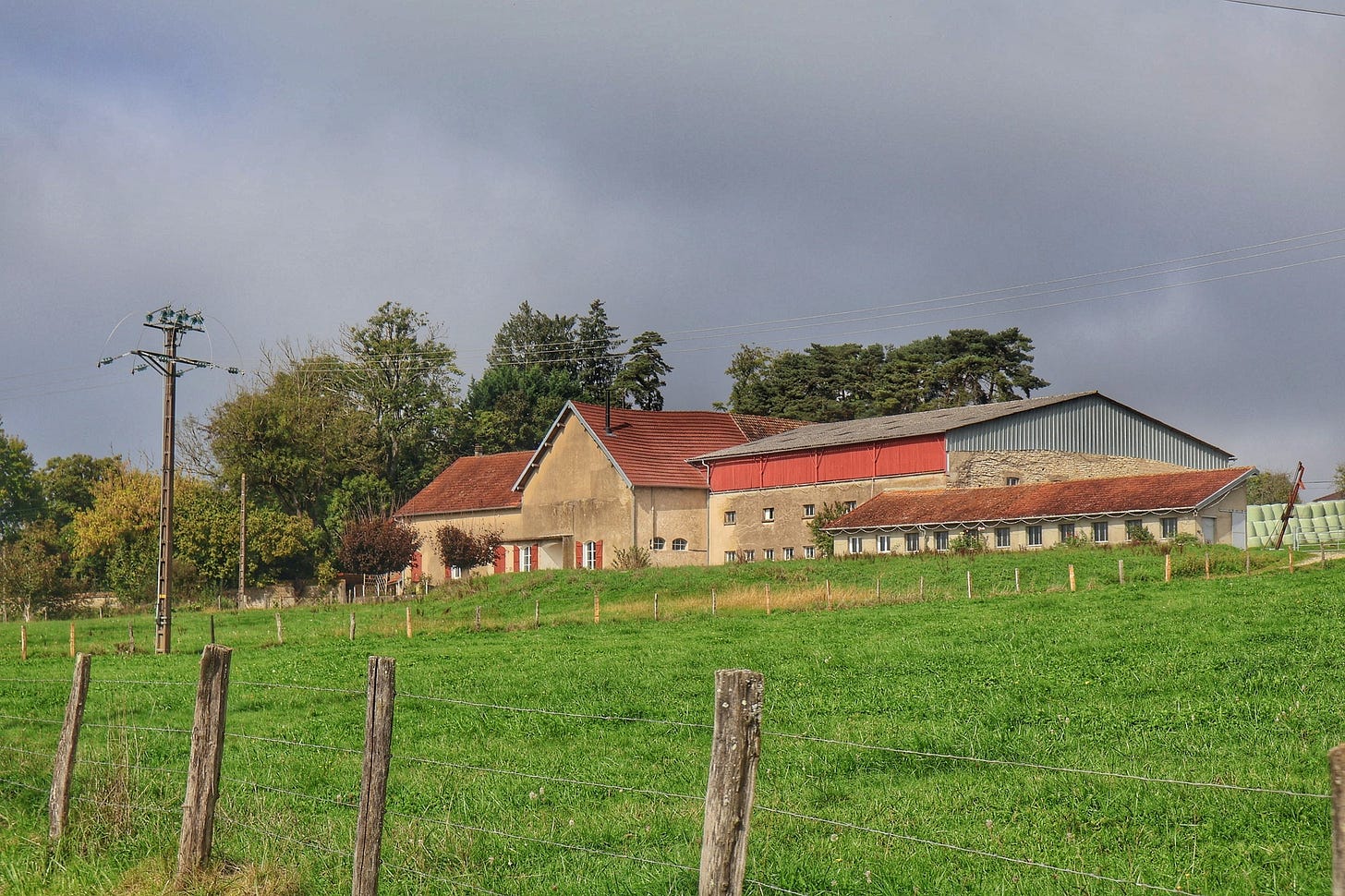 Ancienne ferme familiale du Jura entourée de champs verdoyants sous un ciel nuageux, vestige du monde paysan d’autrefois. Ancienne ferme familiale du Jura entourée de champs verdoyants sous un ciel nuageux, vestige du monde paysan d’autrefois.