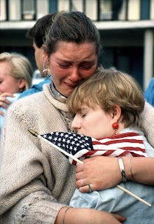 a mother crying as she hugs her child and clutches a small American flag