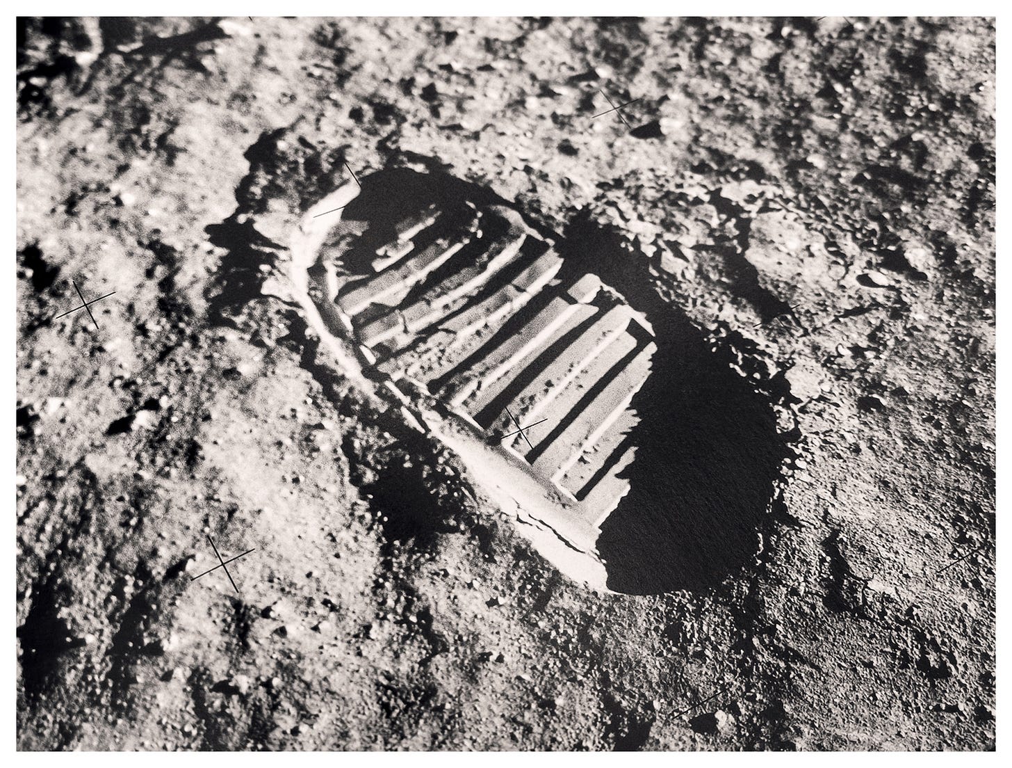 A photograph of a spread from the book Full Moon by Michael Light, reproducing the Apollo 11 bootprint photograph — an astronaut's boot tread pressed into gray lunar soil, reseau cross-marks across the frame. Photograph by Sean Perry for The Sunday Find.