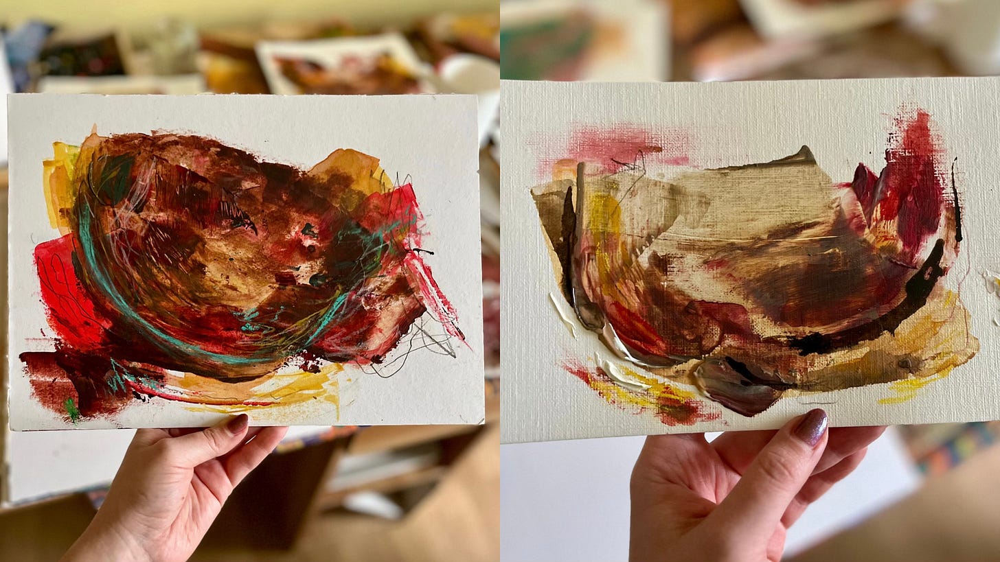 Two small abstract paintings held in each hand against a softly blurred background. The works feature rich, layered textures in earthy reds, browns, and yellows, with expressive brushstrokes and marks. The image captures a sense of intimacy and creative process, highlighting the quiet energy of the pieces.