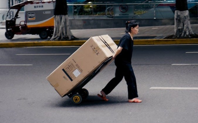 woman in black shirt and pants pulling a large box on a cart behind her