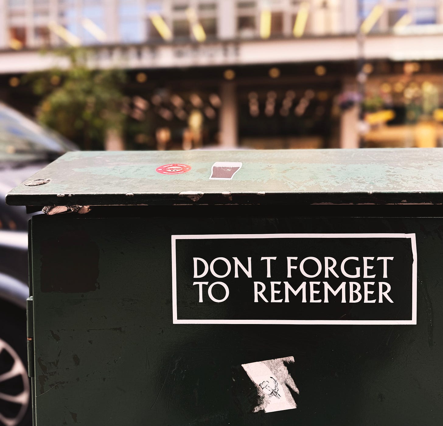 A sticker that says "DON'T FORGET TO REMEMBER" is on an electric box in a city street A sticker that says "DON'T FORGET TO REMEMBER" is on an electric box in a city street