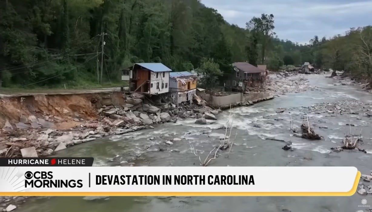 video screenshot of partly-destroyed houses and a road that has collapsed along a riverbank. A verdant wooded hillside behind the wreckage suggests the site's previous beauty. video screenshot of partly-destroyed houses and a road that has collapsed along a riverbank. A verdant wooded hillside behind the wreckage suggests the site's previous beauty.