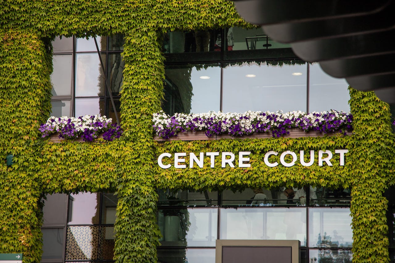 The ivy-covered exterior of Centre Court at Wimbledon with purple and white flowers and the Centre Court sign