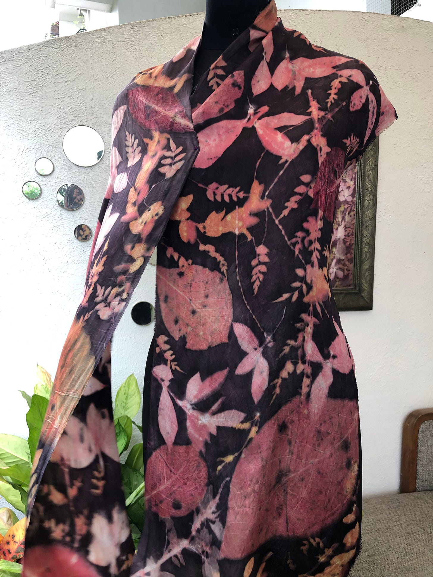 Mannequin draped in a dark eco-printed textile with pink botanical shapes.”