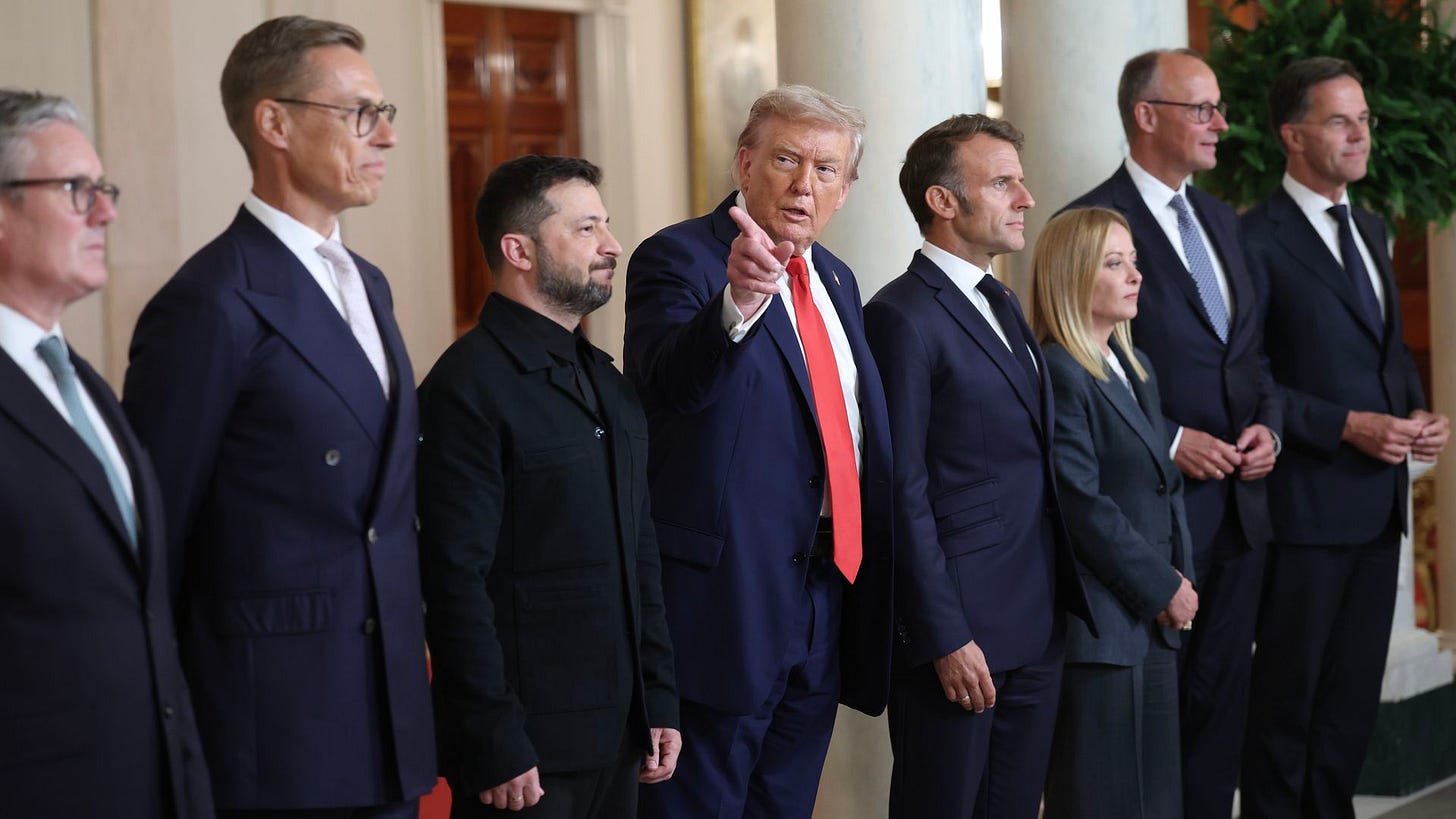 A group of eight formally dressed politicians and leaders stand indoors. One man in the center wearing a navy suit and red tie is pointing. The others wear dark suits or jackets. A group of eight formally dressed politicians and leaders stand indoors. One man in the center wearing a navy suit and red tie is pointing. The others wear dark suits or jackets.