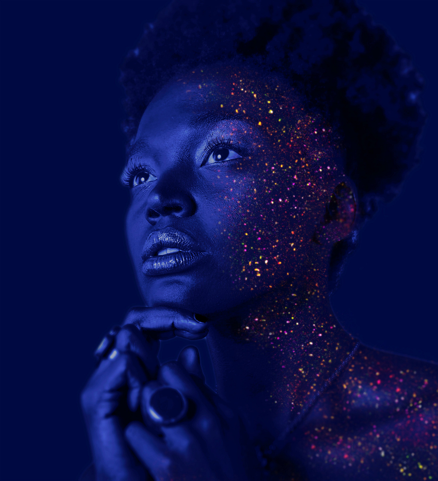 A young woman under black light with glowing paint spattered on her face.