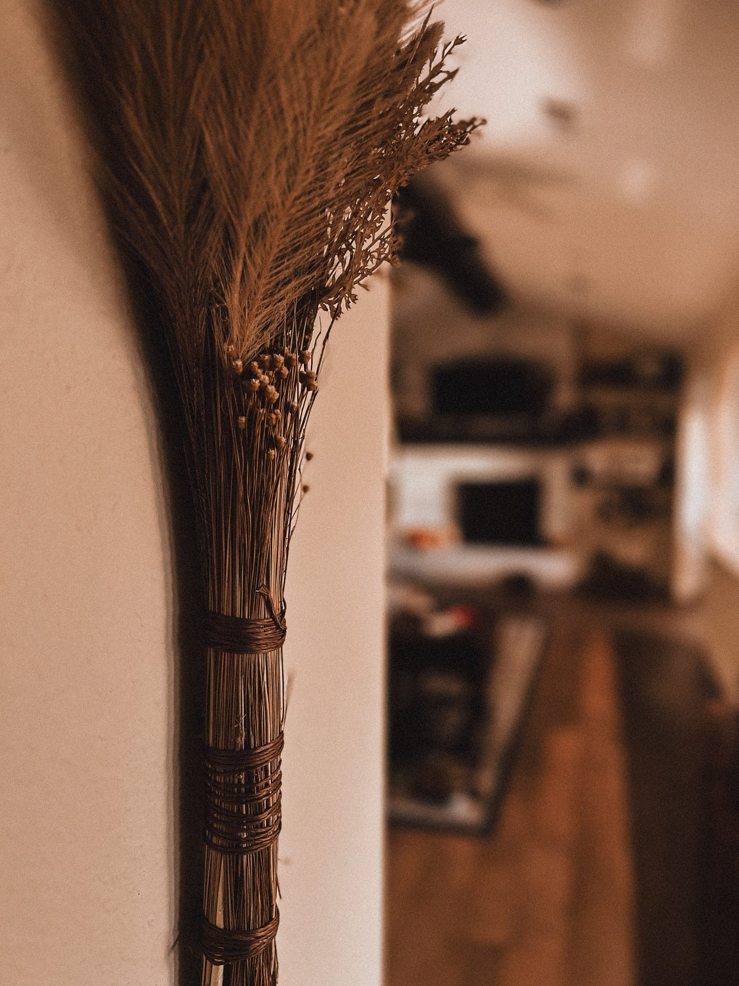 A close-up shot of a decorative broom hanging on a wall, with the rest of Sarah's living room in the background.