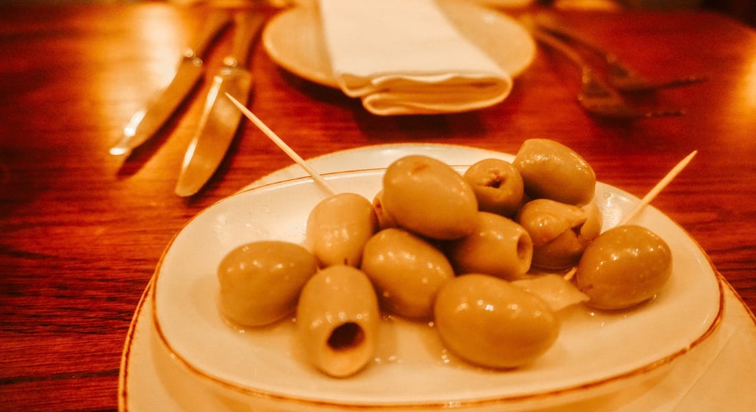 A white bowl with olives on a wooden table A white bowl with olives on a wooden table