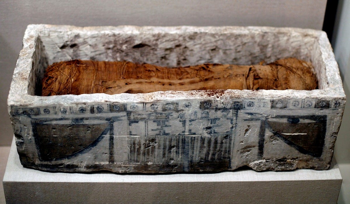 An aged stone box, decorated with paint on the sides, open at the top, with a small linen-wrapped form within.