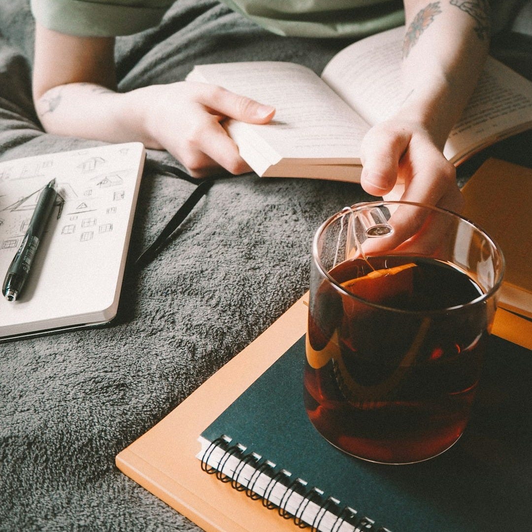 a person sitting on a bed with a book and a drink a person sitting on a bed with a book and a drink