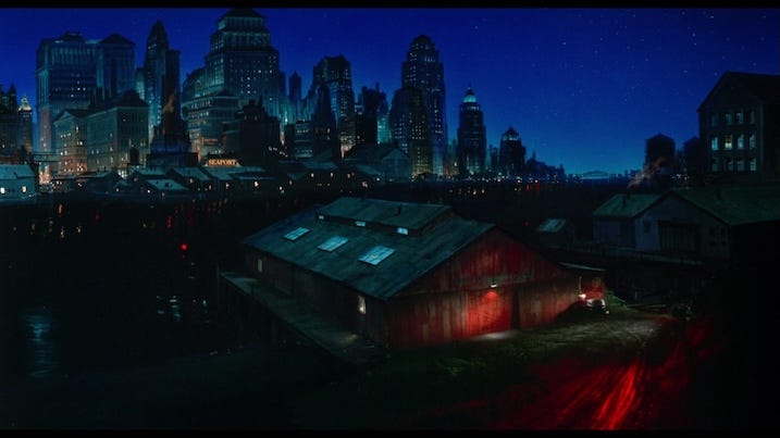 A sweeping matte painting of the fictional city skyline at night, with glowing lights reflecting on the water—showcasing the film’s comic strip aesthetic.