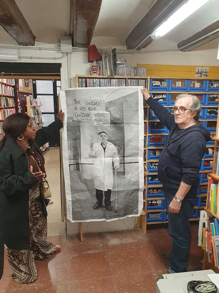 Storefront of the Bookshop in red and black, and a foto of a Black woman and a white man holding a poster between them, surrounded by books. 