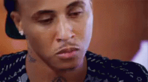 A close-up of a person looking down with a restrained, emotional expression, appearing to shed a single tear.