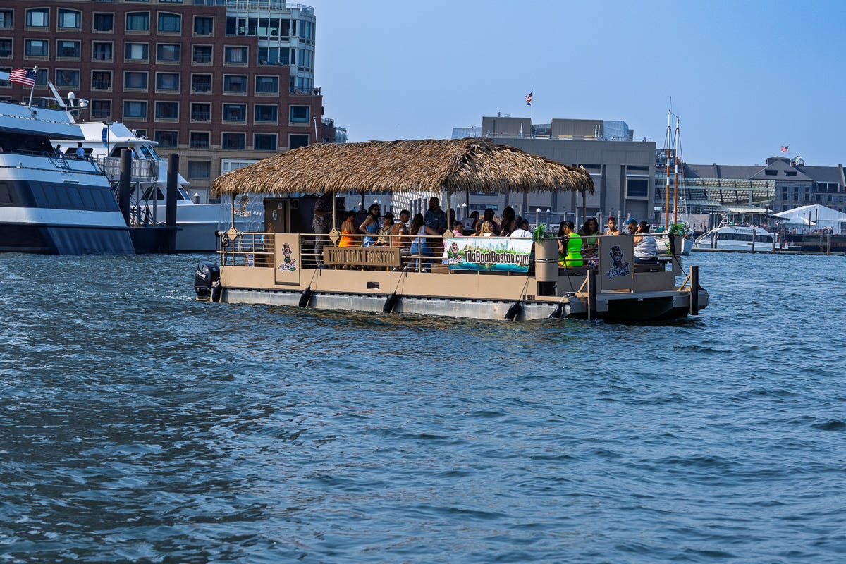 Large tiki-style party boat filled with people cruising through Boston Harbor