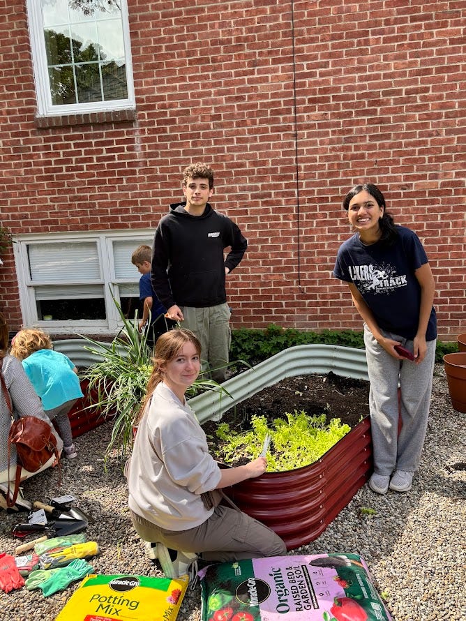 Three teenagers cleaning up a planter bed.