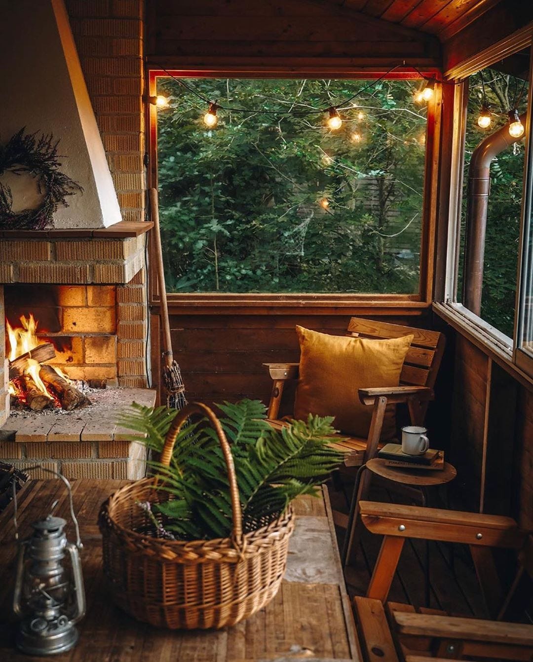 Warm and inviting screened porch with a brick fireplace, wooden furniture, and string lights overlooking forest views.