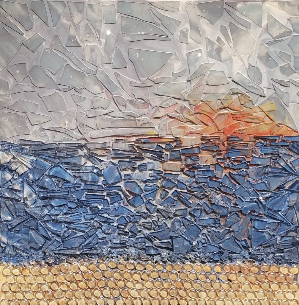 Seascape with a setting sun in the distance. Mixed media in acrylic and glass. A gray sky is in the back with an orange sunset. In the middle is a blue calm ocean. At the base is sand with round glass stones. Original artwork by Anna Loscotoff.
