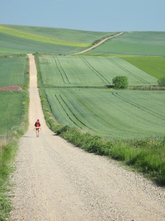 This may contain: a person riding a bike down a dirt road in the middle of an open field