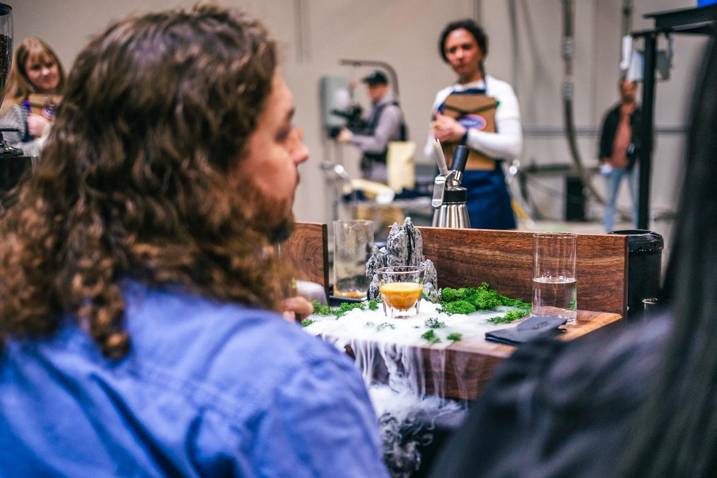 a signature beverage from morgan eckroth sits at the judges table, with a judge looking on. the beverage fogs dramatically from dry ice.