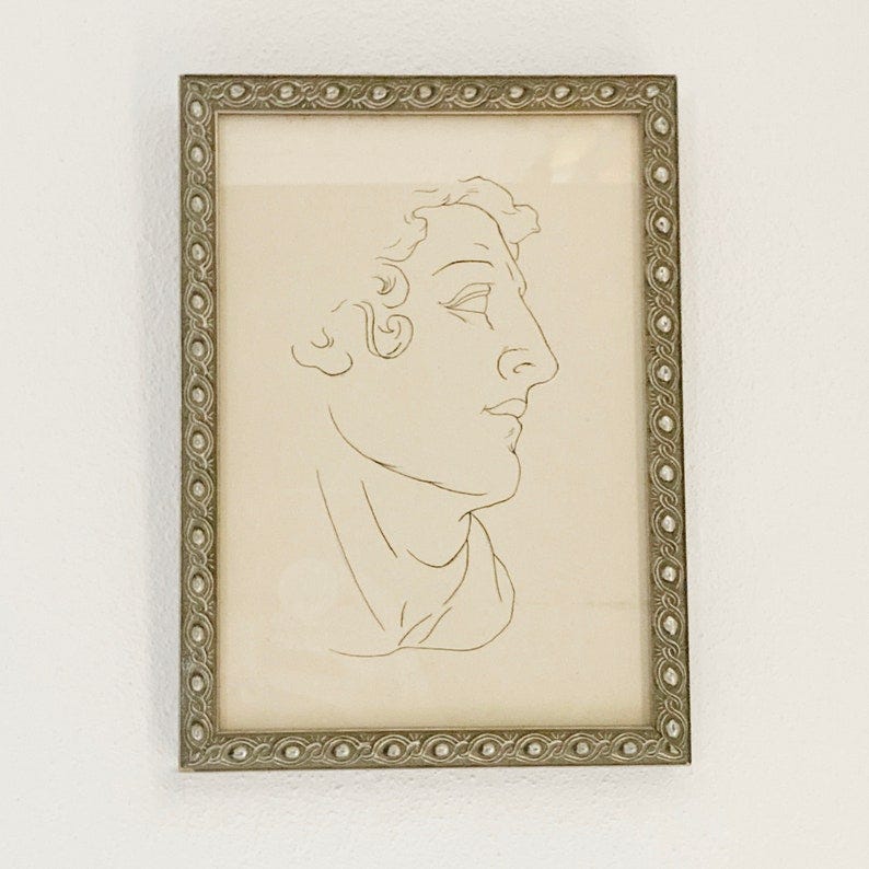 May include: A framed black and white line drawing of a person's face in profile. The frame is silver with a decorative border.