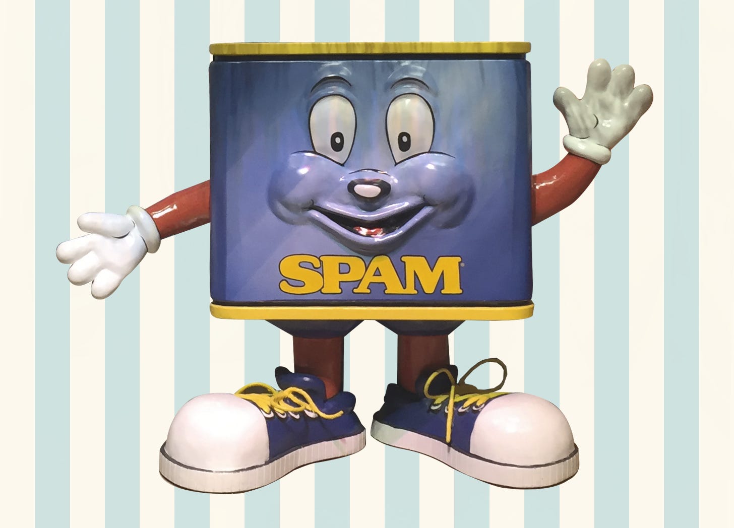 Big statue of a characterized SPAM can wearing blue tennis shoes, on a cream and seafoam green stripe background