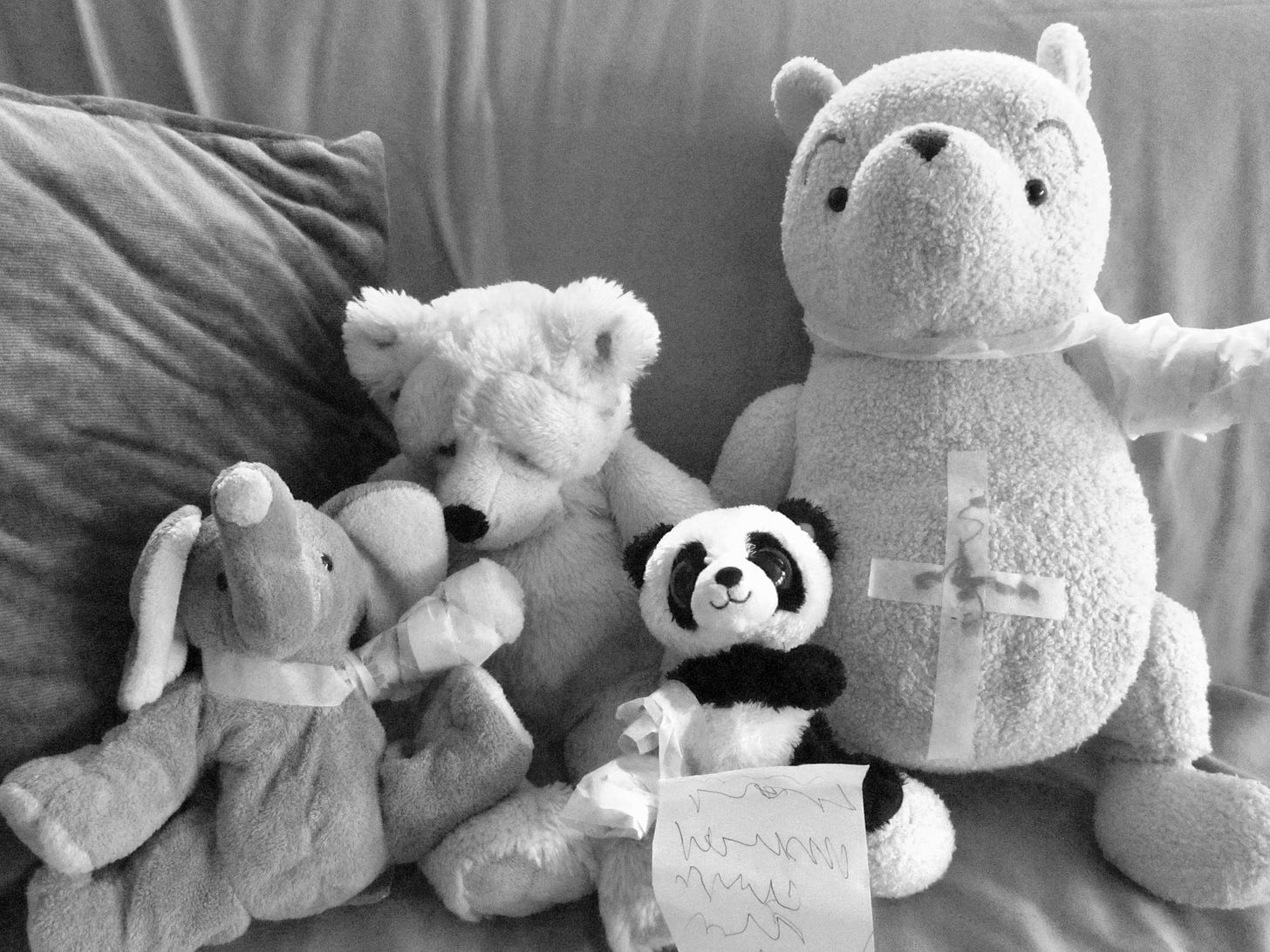Stuffed elephant and bears wearing tape bandages with child's scribbled prescription