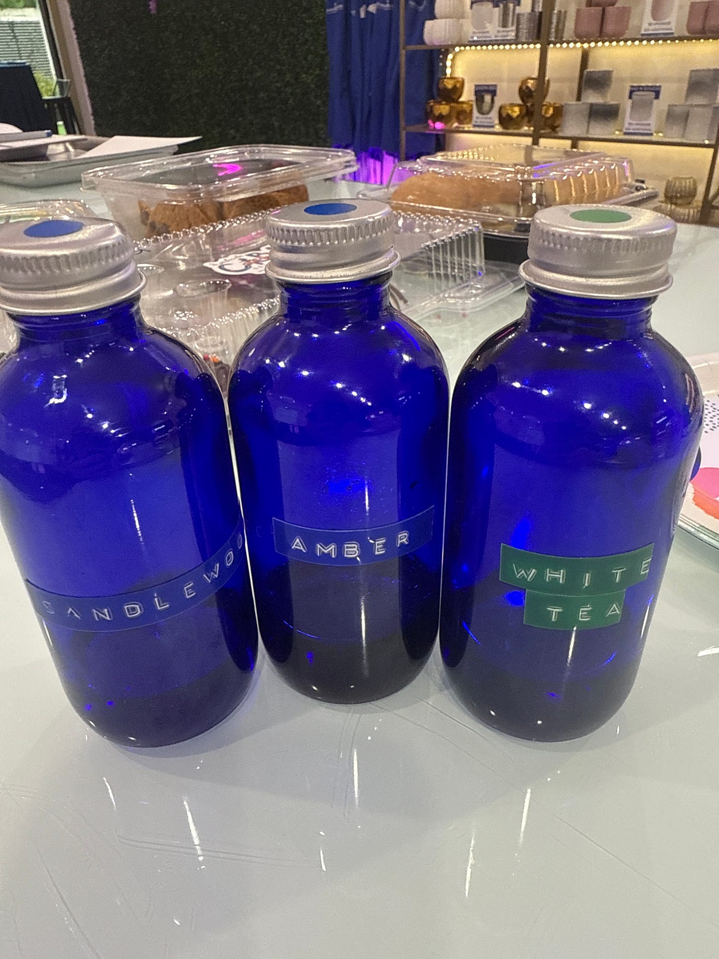 Three blue glass bottles with label maker labels reading 'Sandalwood,' 'Amber,' and 'White Tea' sitting on a counter