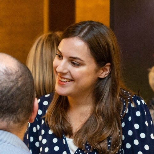A white woman with long brown hair wearing a navy and white spotted dress