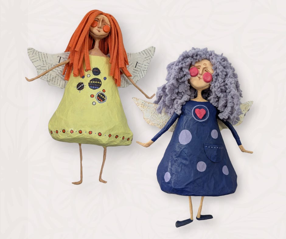 Two handmade mixed-media papier-mâché angel dolls by Stacy Vajta, with clay faces, painted dresses, yarn hair, wire limbs, and decorative wings.