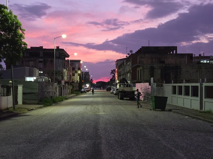 Purple sunset seen down darkening city street.