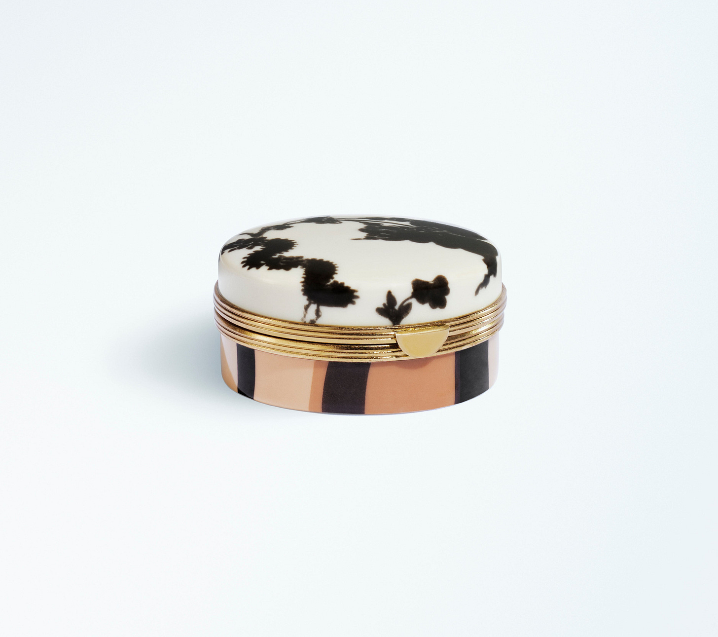 Closed round lip balm compact with a lid featuring black abstract floral motifs, gold-tone trim and a striped beige and black case