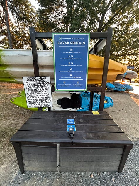 The left image shows a storage rack of eight blue, yellow, and gray kayaks for rent. The middle image shows a QR kayak checkout station, with a blue sign, a white sign letting Nicole know she can't sue Arkansas State Parks if she drowns, and a brown lockbox that holds oars and lifejackets. The final image is the sweet view of freedom: the front tip of a lime-green kayak is visible above a large lake of soft, deep blue waves.