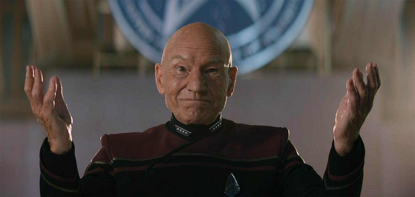 This image shows Admiral Jean-Luc Picard (played by Patrick Stewart) holding his hands apart and facing upward as he addressed Starfleet Academy's second-year cadets. The lower portion of the academy's flag is visible behind Picard. This image shows Admiral Jean-Luc Picard (played by Patrick Stewart) holding his hands apart and facing upward as he addressed Starfleet Academy's second-year cadets. The lower portion of the academy's flag is visible behind Picard.