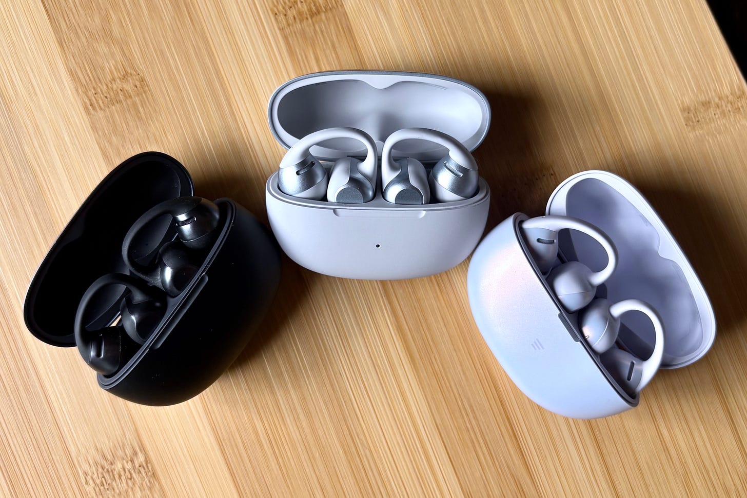 Shokz OpenDots One, OpenDots 2, and OpenDots Air, arranged in a semi-circle with charging lids open. Shokz OpenDots One, OpenDots 2, and OpenDots Air, arranged in a semi-circle with charging lids open.